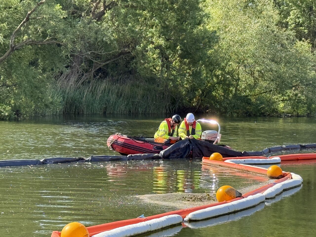 Two crew in an inflatable workboat fixing a silt curtain and oil boom in the river
