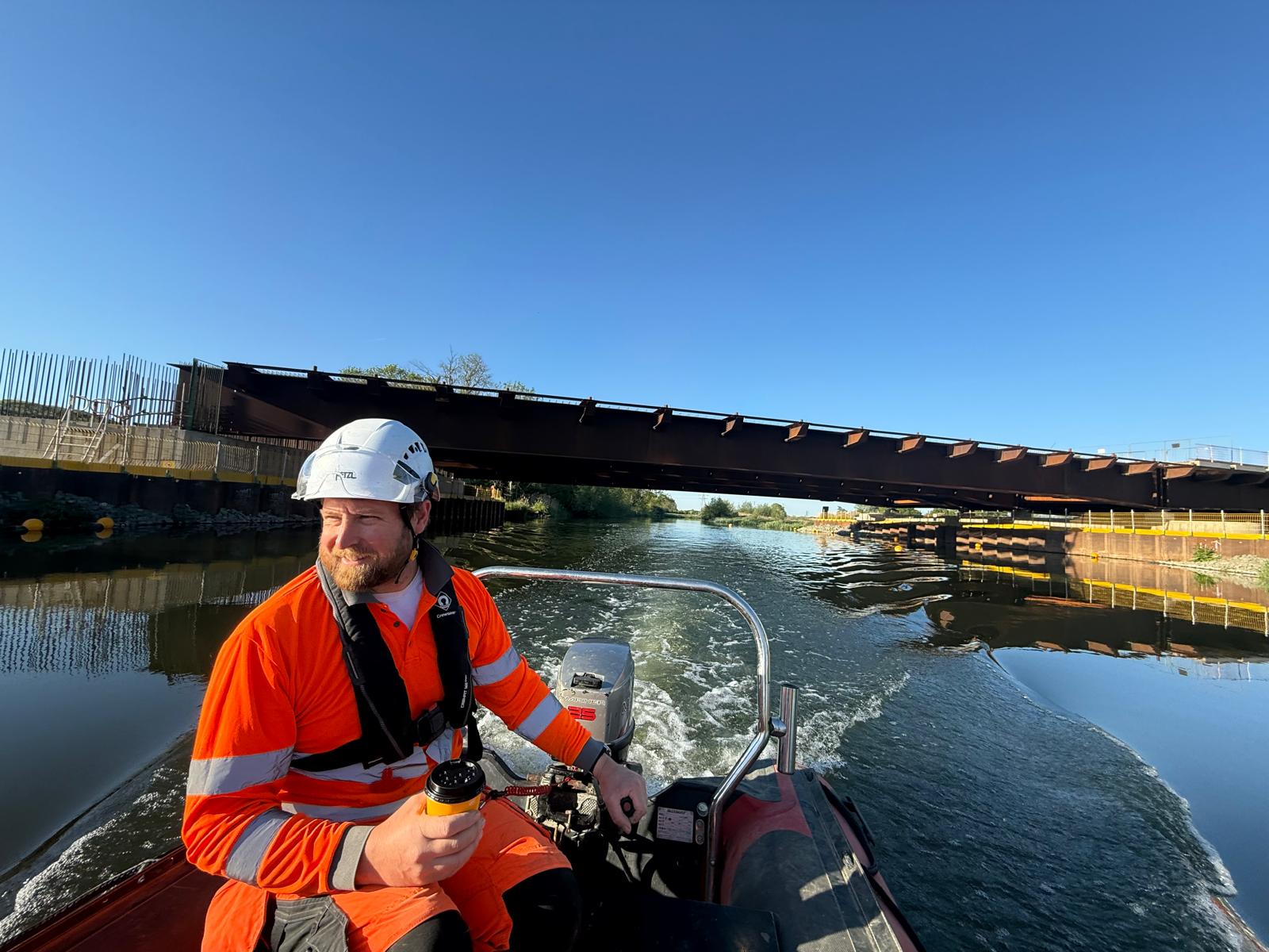 RYA-qualified boat operator steering a safety boat beneath a bridge on a sunny day