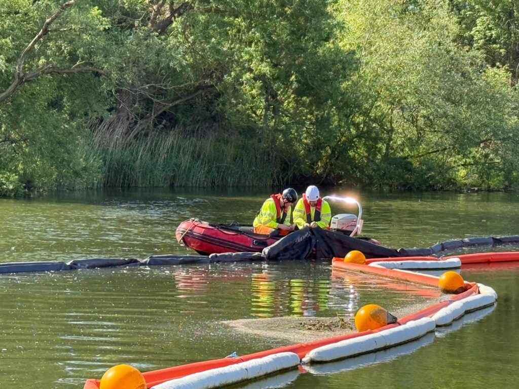 Two boat crew working from an inflatable workboat to set out floating booms on a river